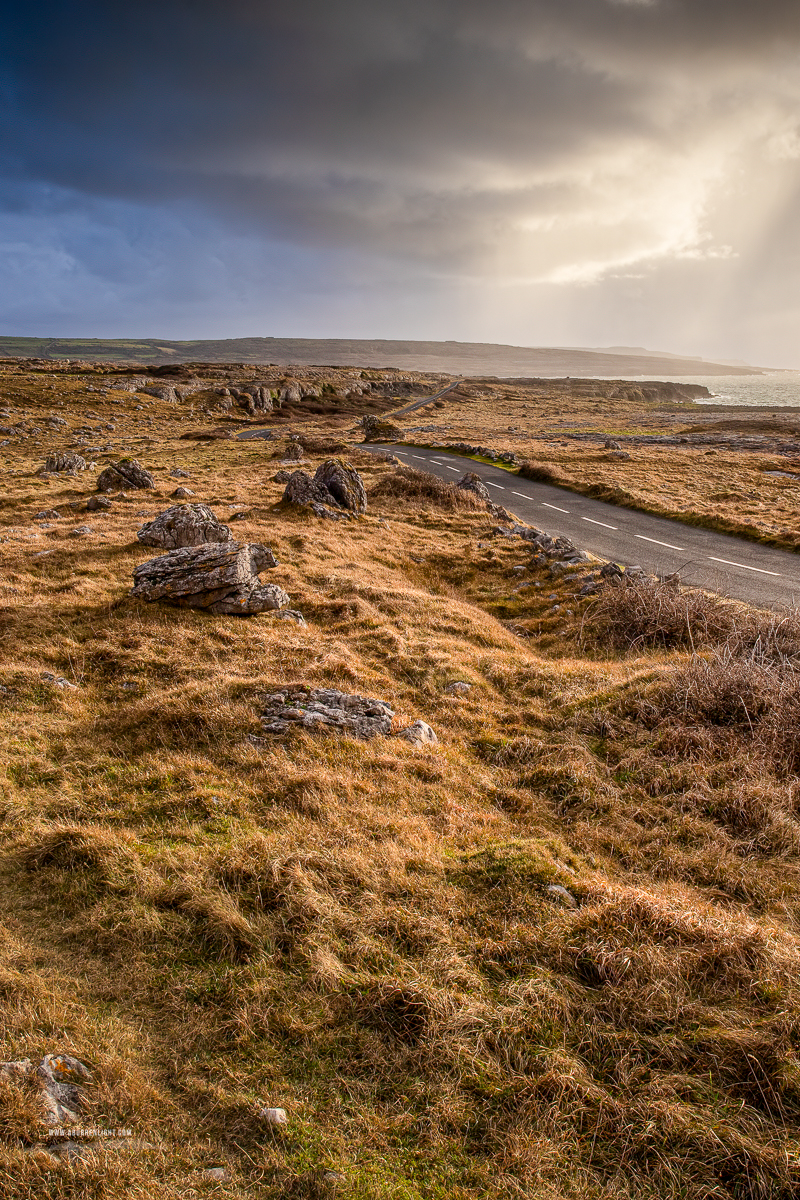 A narrow track crossing golden winter grass and exposed limestone beneath dramatic storm clouds near Fanore