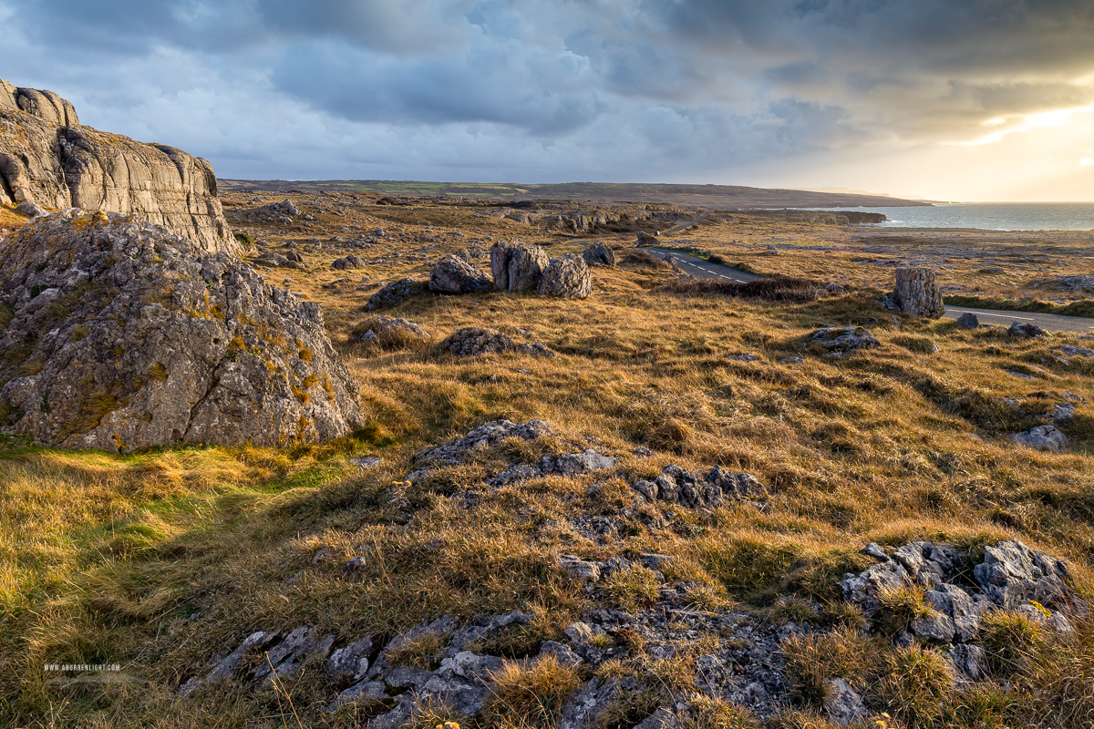 Large weathered limestone boulders amid winter grass beneath dramatic sunset clouds near Fanore, County Clare.
