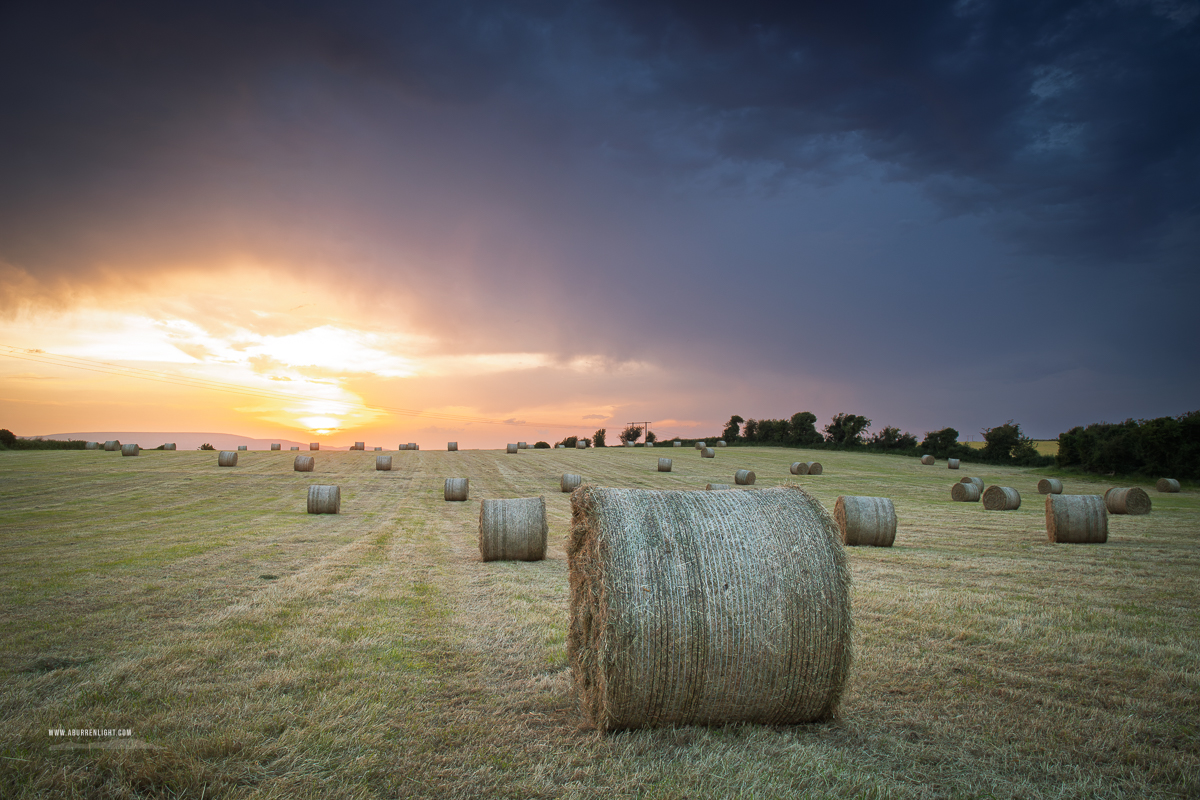 Freshly harvested field with hay bales under colourful sunset skies in County Galway.