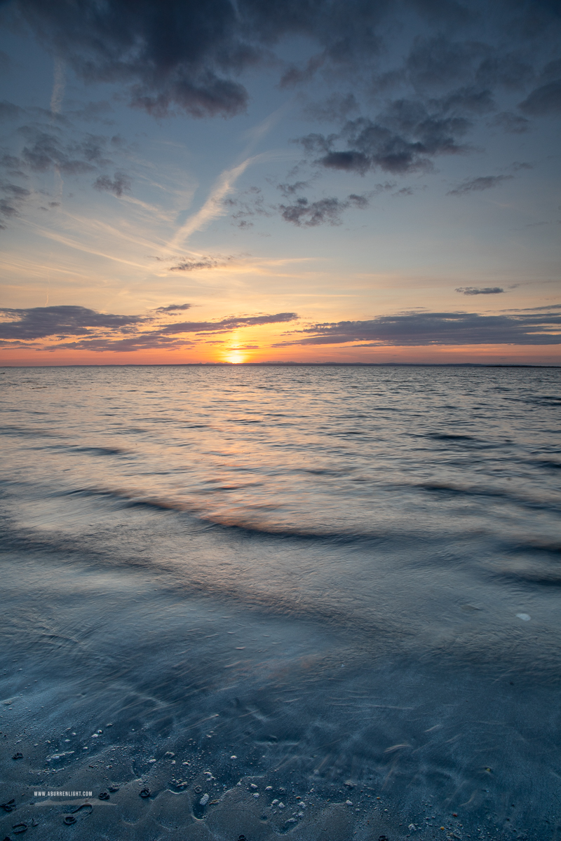 Soft blue waves wash across Traught Beach as the setting sun glows along the distant horizon near Kinvara.