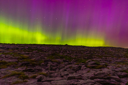 A vivid green auroral band and purple curtains glowing above a broad limestone ridge at Fahee North in the Burren.