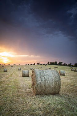 Hay bale beneath dark storm clouds glowing with warm sunset light near Gort, County Galway.