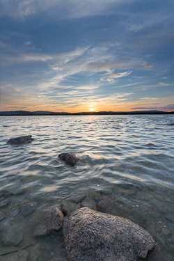 A limestone boulder rises from rippled blue water beneath a sweeping summer sunset sky at Lough Bunny, County Clare.