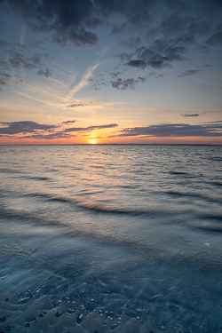 Soft blue waves wash across Traught Beach as the setting sun glows along the distant horizon near Kinvara.